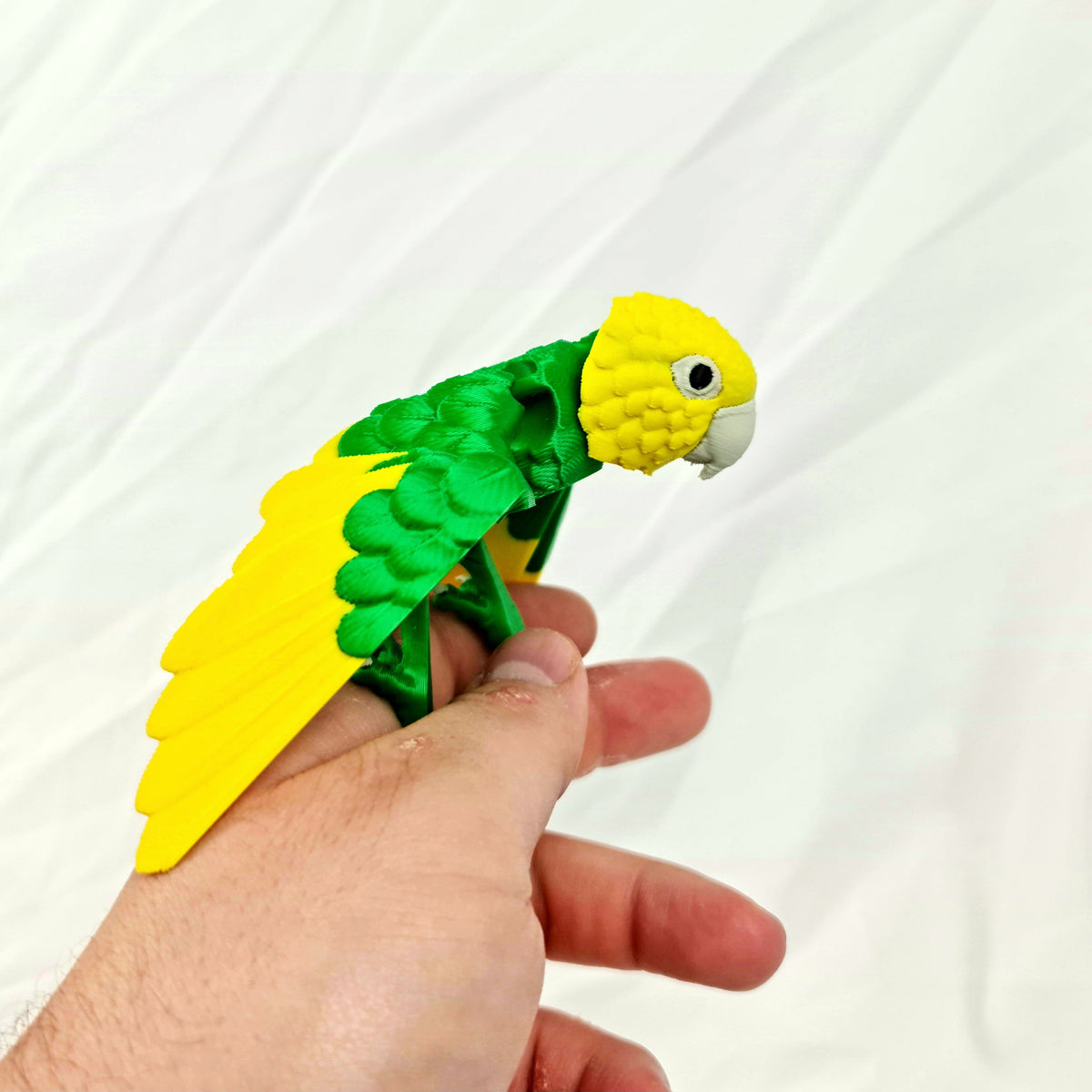 Gele en groene 3D-geprinte beweegbare dwergpapegaai vastgehouden in een hand voor formaatindicatie