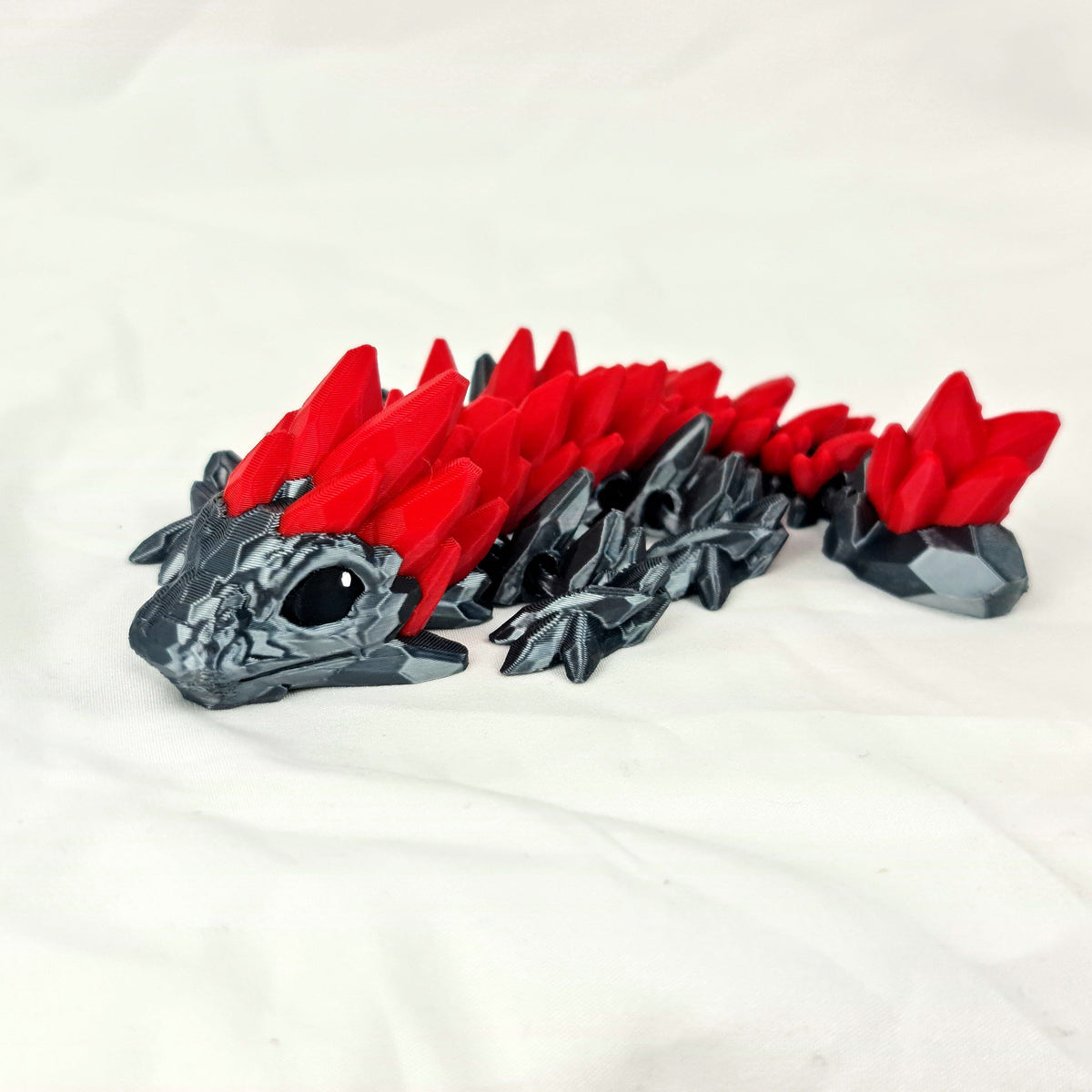 Overzicht van de gelede 3D-geprinte zwart-rode gemstone baby draak op een witte stof.