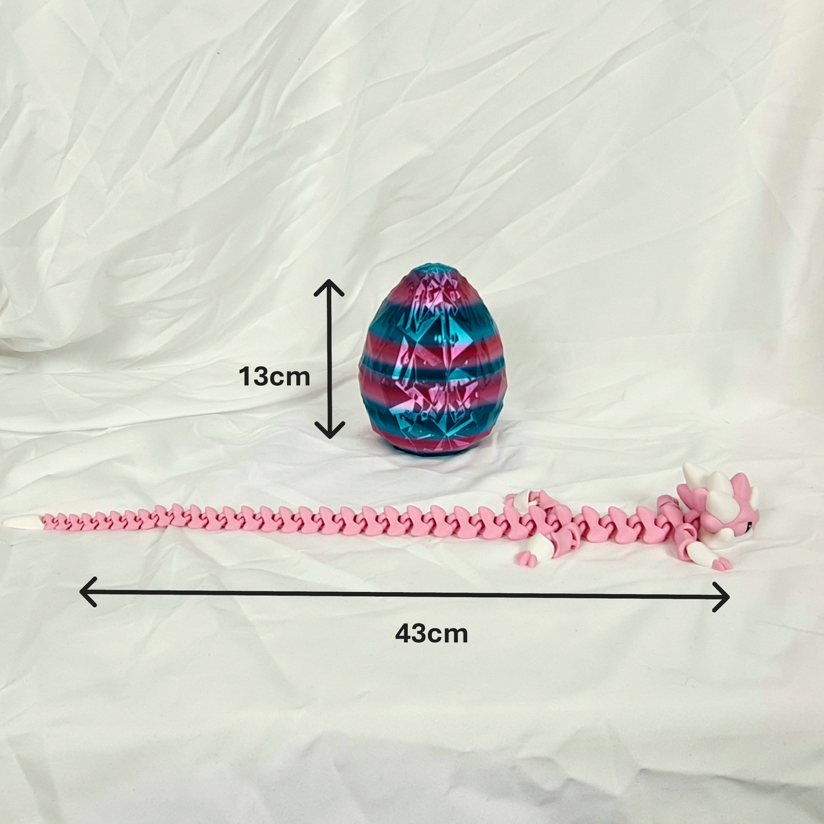 Zijaanzicht van de gelede roze baby draak en het roze-blauwe draakenei met maataanduidingen in centimeters.