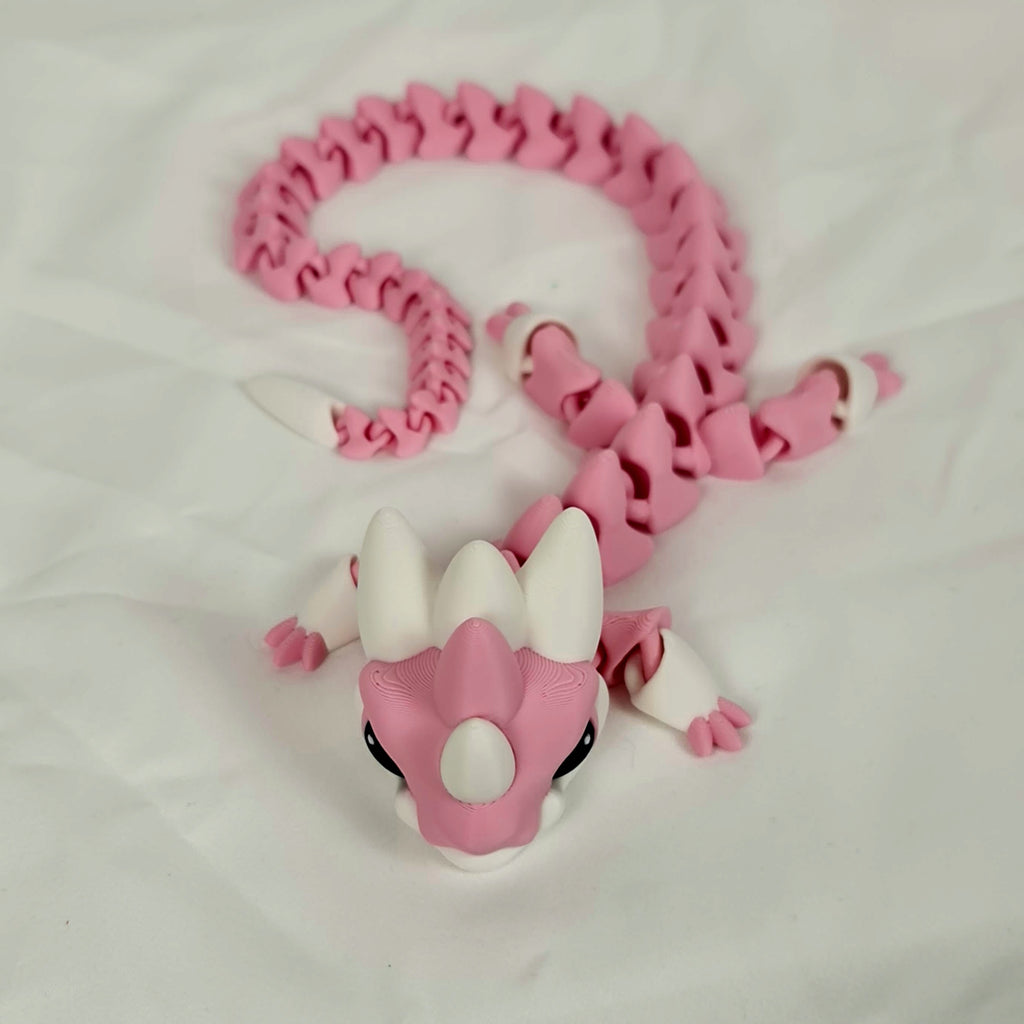 Vooraanzicht van de liggende roze baby draak met witte hoorntjes op een neutrale ondergrond.