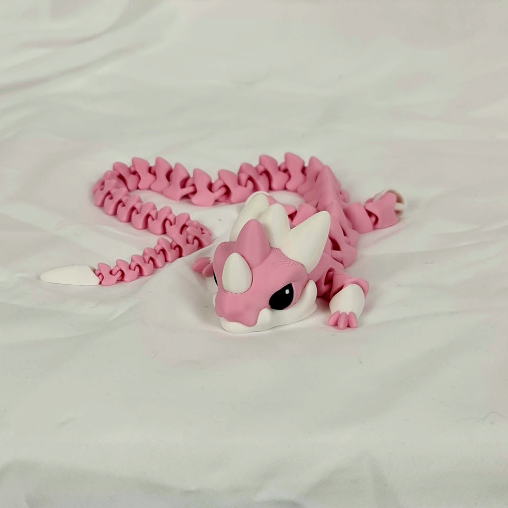 Vooraanzicht van de liggende roze baby draak met witte hoorntjes op een neutrale ondergrond.