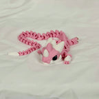 Vooraanzicht van de liggende roze baby draak met witte hoorntjes op een neutrale ondergrond.