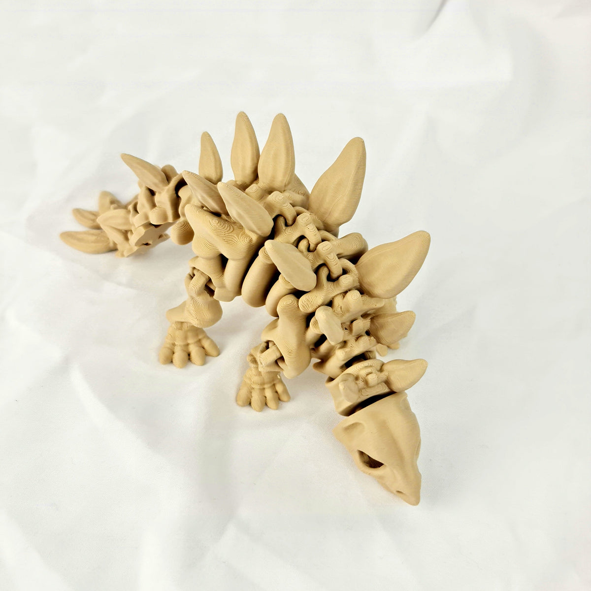 Hoge hoek opname van de beige 3D-geprinte skelet stegosaurus rustend op een witte achtergrond.