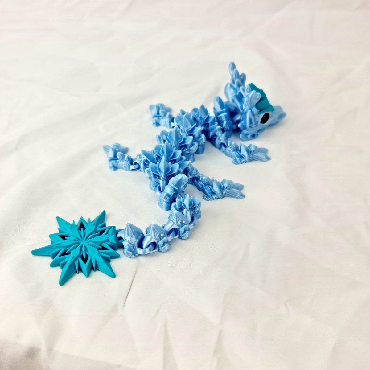Schuin bovenaanzicht van het buigzame lichaam van de lichtblauwe winter baby draak met sneeuwvlokstaart.