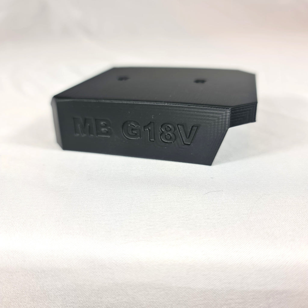 Close-up opname van de losse 3D-geprinte zwarte wandhouder en opbergbeugel voor Makita G-Series 18V accu's op witte stof