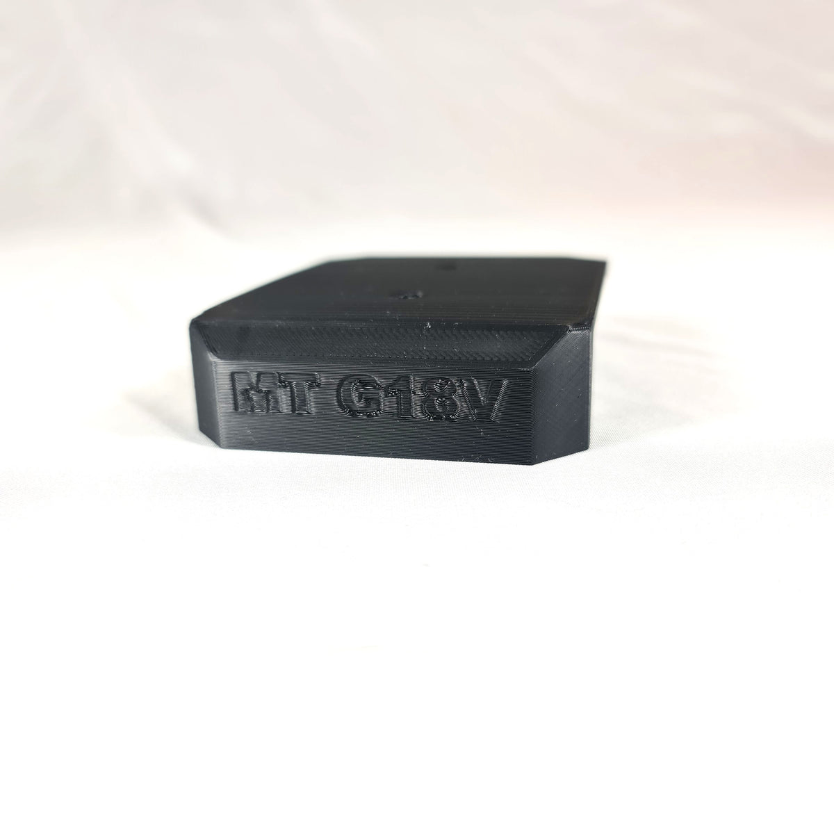 Close-up opname van de losse 3D-geprinte zwarte wandhouder voor Makita G-Series 18V apparatuur op witte stof