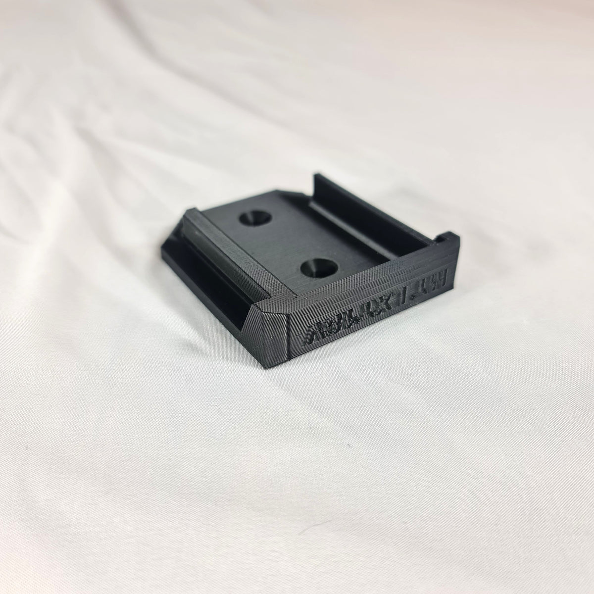 Close-up opname van de losse 3D-geprinte zwarte wandhouder en gereedschapssteun voor Makita LXT 18V apparatuur op witte stof