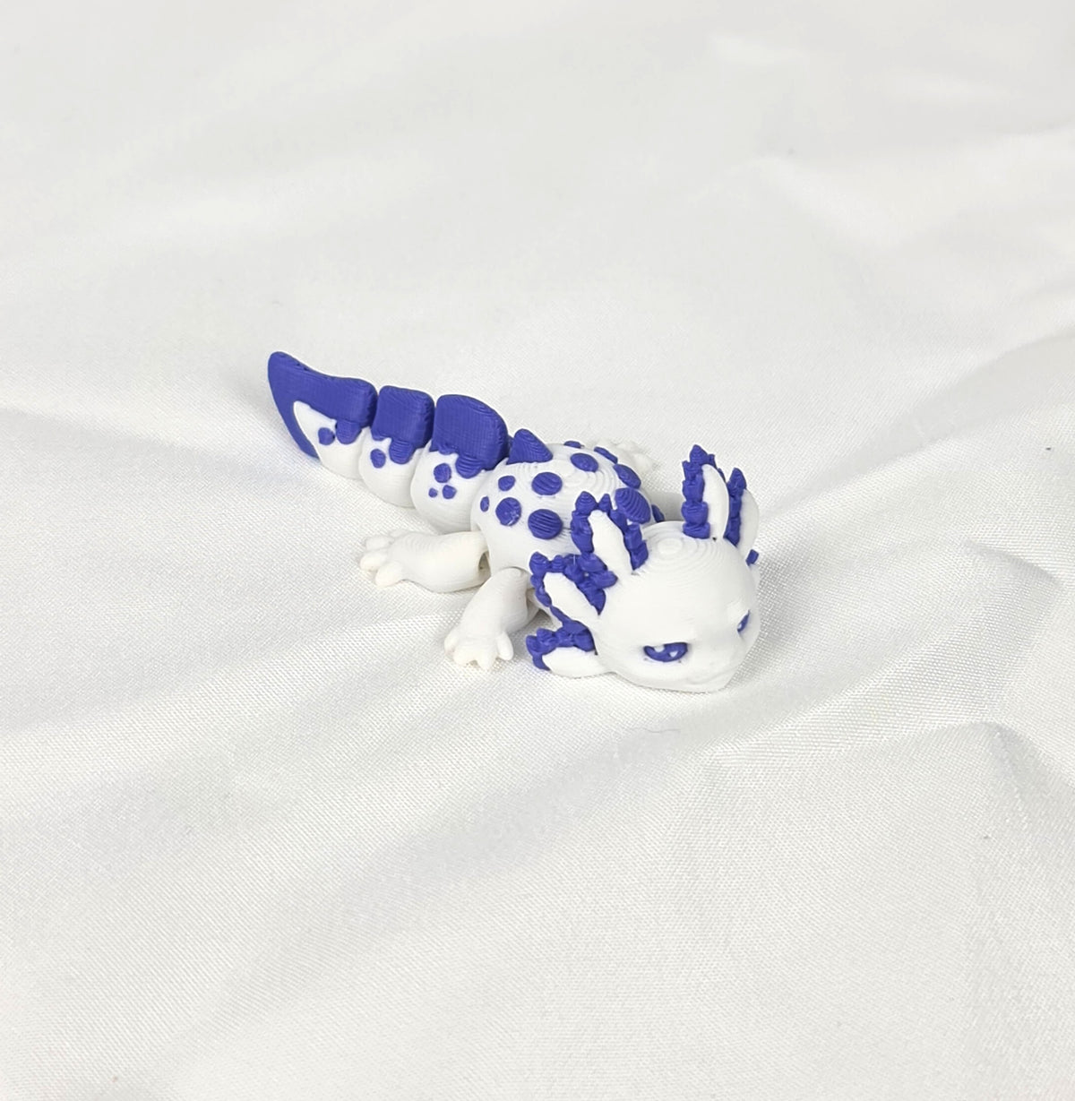 Close-up opname van de gedetailleerde paarse kieuwen en het flexibele lijf van de handgemaakte 3D-geprinte axolotl op witte stof