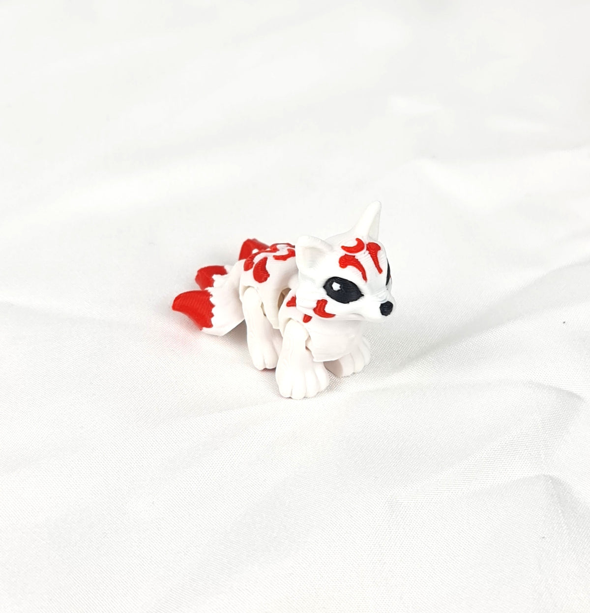 Close-up opname van de gedetailleerde rode patronen en de flexibele staart van de handgemaakte 3D-geprinte Kitsune op witte stof