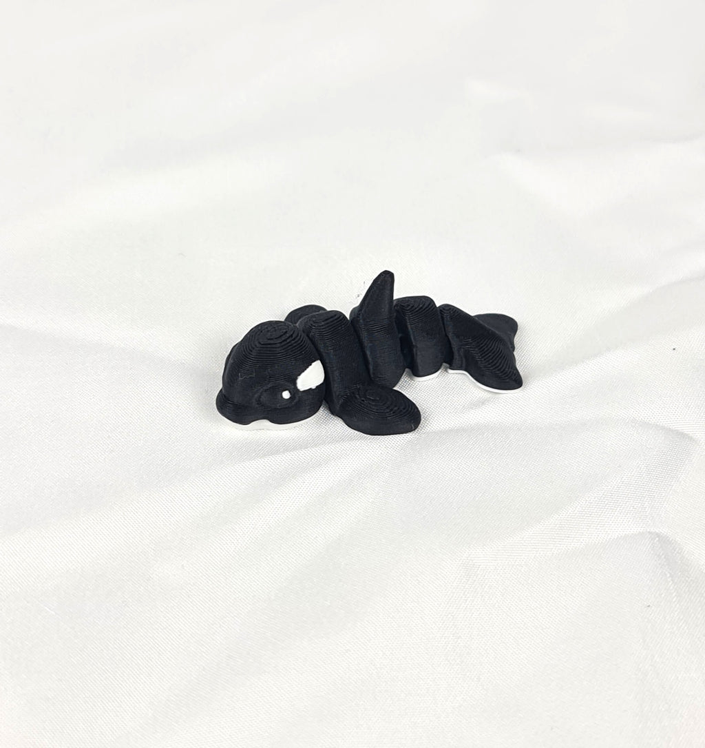 Close-up opname van de karakteristieke rugvin en het flexibele zwarte lijf van de handgemaakte 3D-geprinte orca op witte stof