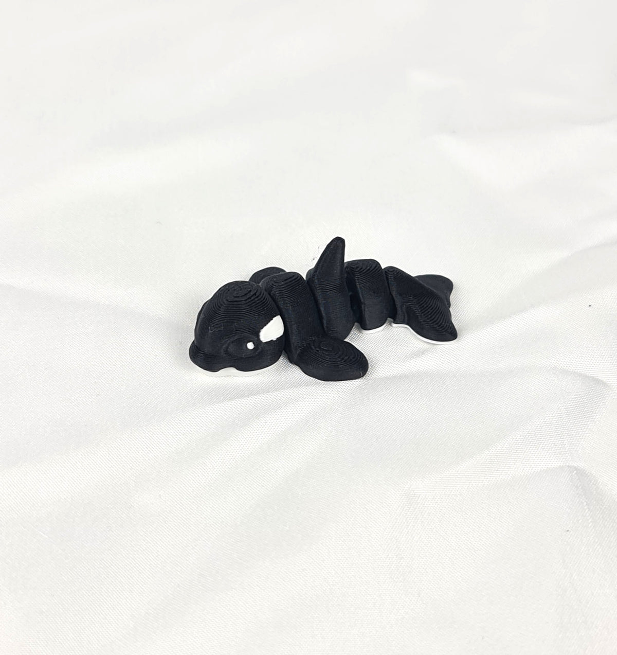 Close-up opname van de karakteristieke rugvin en het flexibele zwarte lijf van de handgemaakte 3D-geprinte orca op witte stof