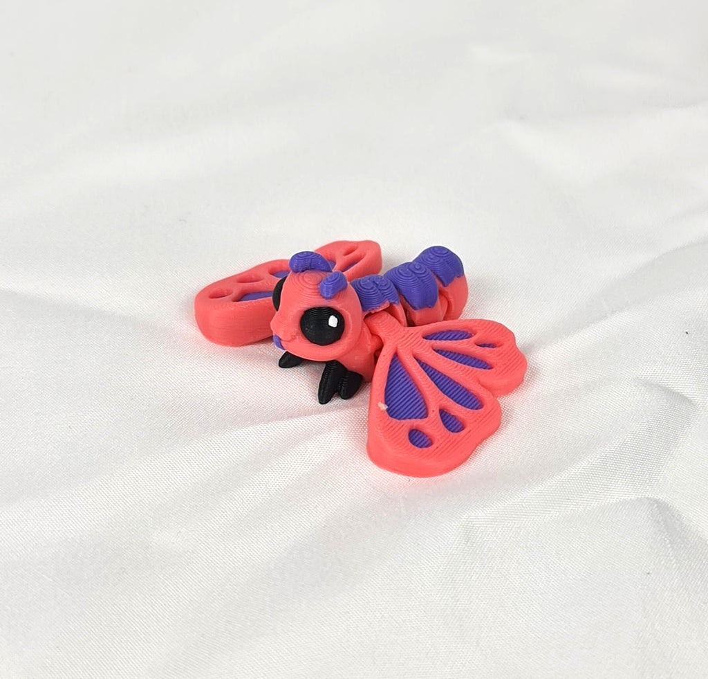 Close-up opname van de ingewikkelde vleugelstructuur van de roze-paarse 3D-geprinte flexibele vlinder op een wit textieloppervlak.