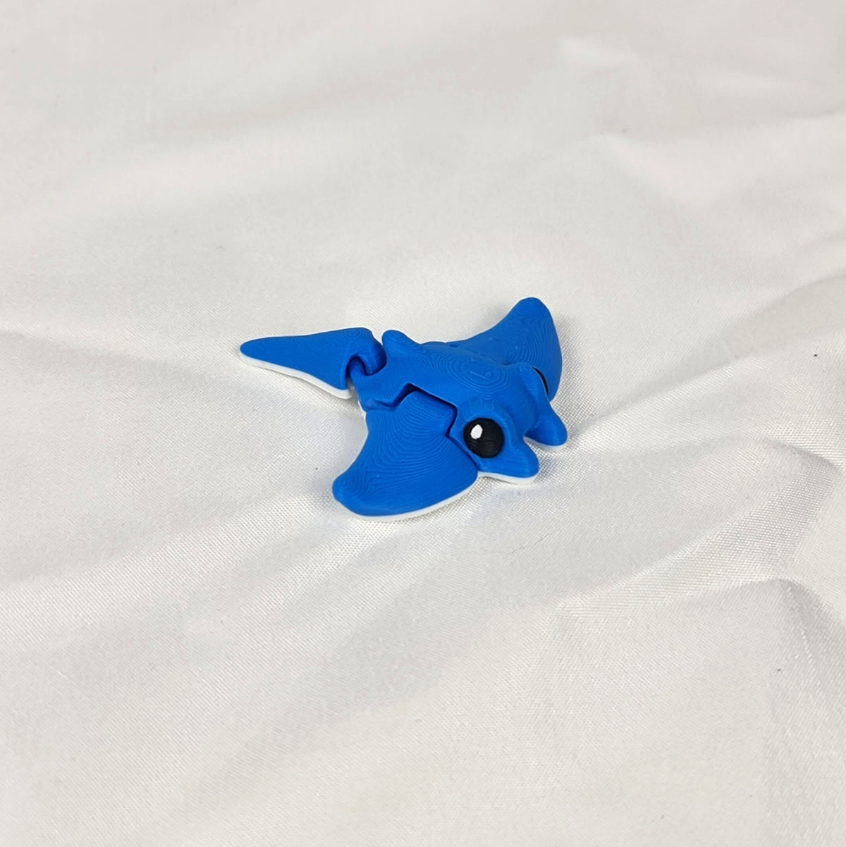 Close-up van een flexibele blauwe mini mantarog 3D-print op een witte ondergrond