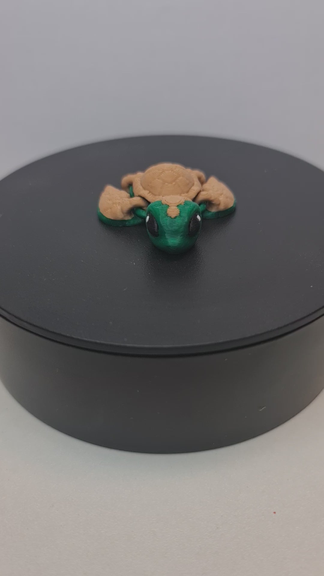 Video still van de 3D-geprinte flexibele schildpad die ronddraait op een zwarte draaitafel, tonend de volledige beweegbaarheid.