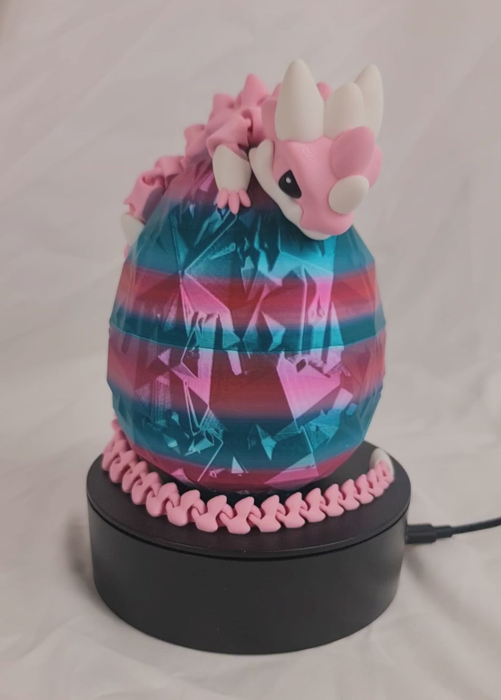 Video van de flexibele roze baby draak gewikkeld om een metallic roze-blauw ei op een draaibaar platform.