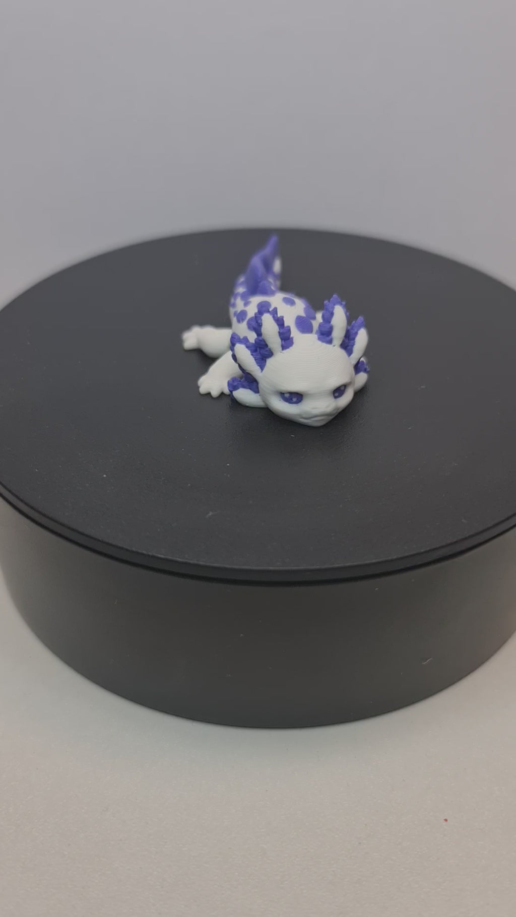 Close-up opname van de gedetailleerde paarse kieuwen en het flexibele lijf van de handgemaakte 3D-geprinte axolotl op witte stof