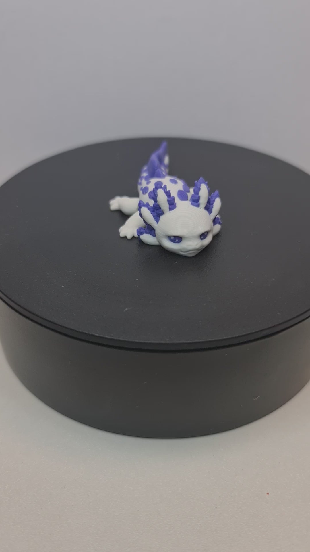 Close-up opname van de gedetailleerde paarse kieuwen en het flexibele lijf van de handgemaakte 3D-geprinte axolotl op witte stof