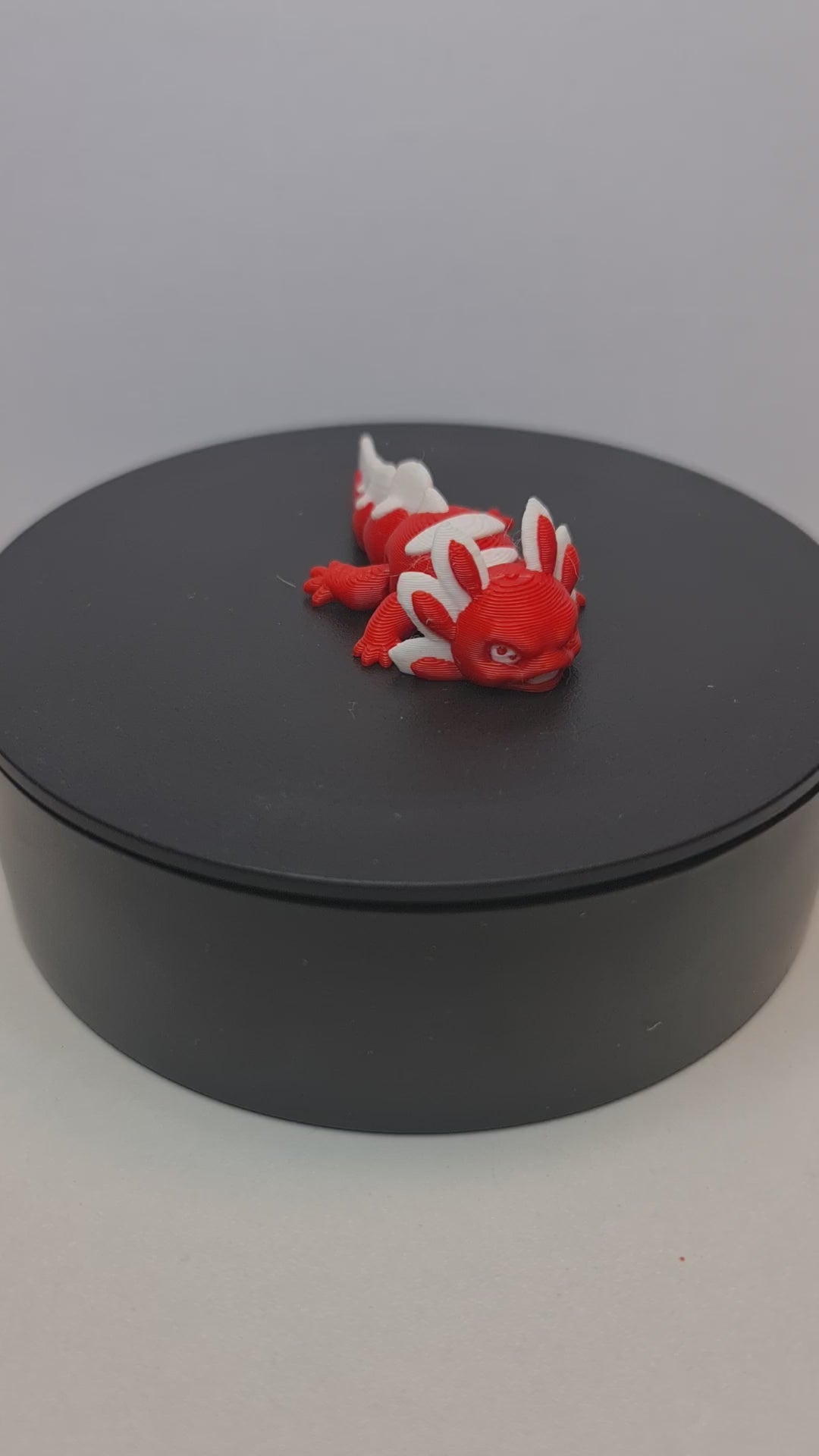 Video still van de flexibele 3D-geprinte mini axolotl Ruby die ronddraait op een zwarte draaitafel om de beweegbare gewrichten te tonen