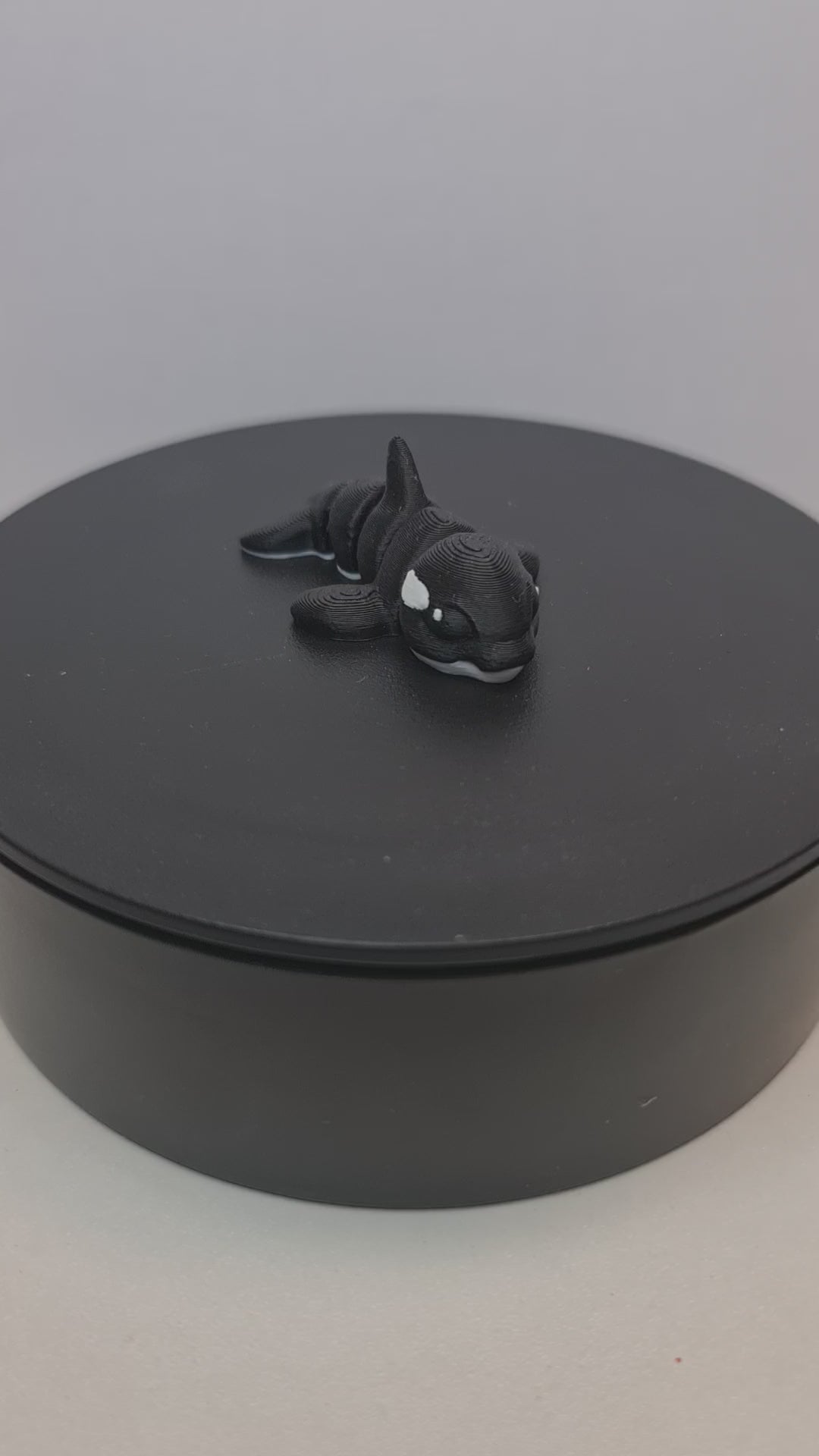 Video still van de flexibele 3D-geprinte mini orca die ronddraait op een zwarte draaitafel om de beweegbare gewrichten te tonen