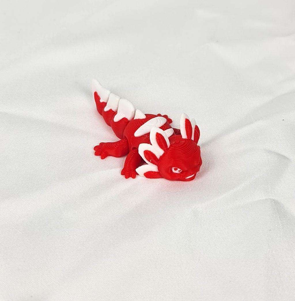 De rode en witte 3D-geprinte flexibele mini axolotl Ruby gefotografeerd vanuit een schuine hoek als decoratief kunstobject