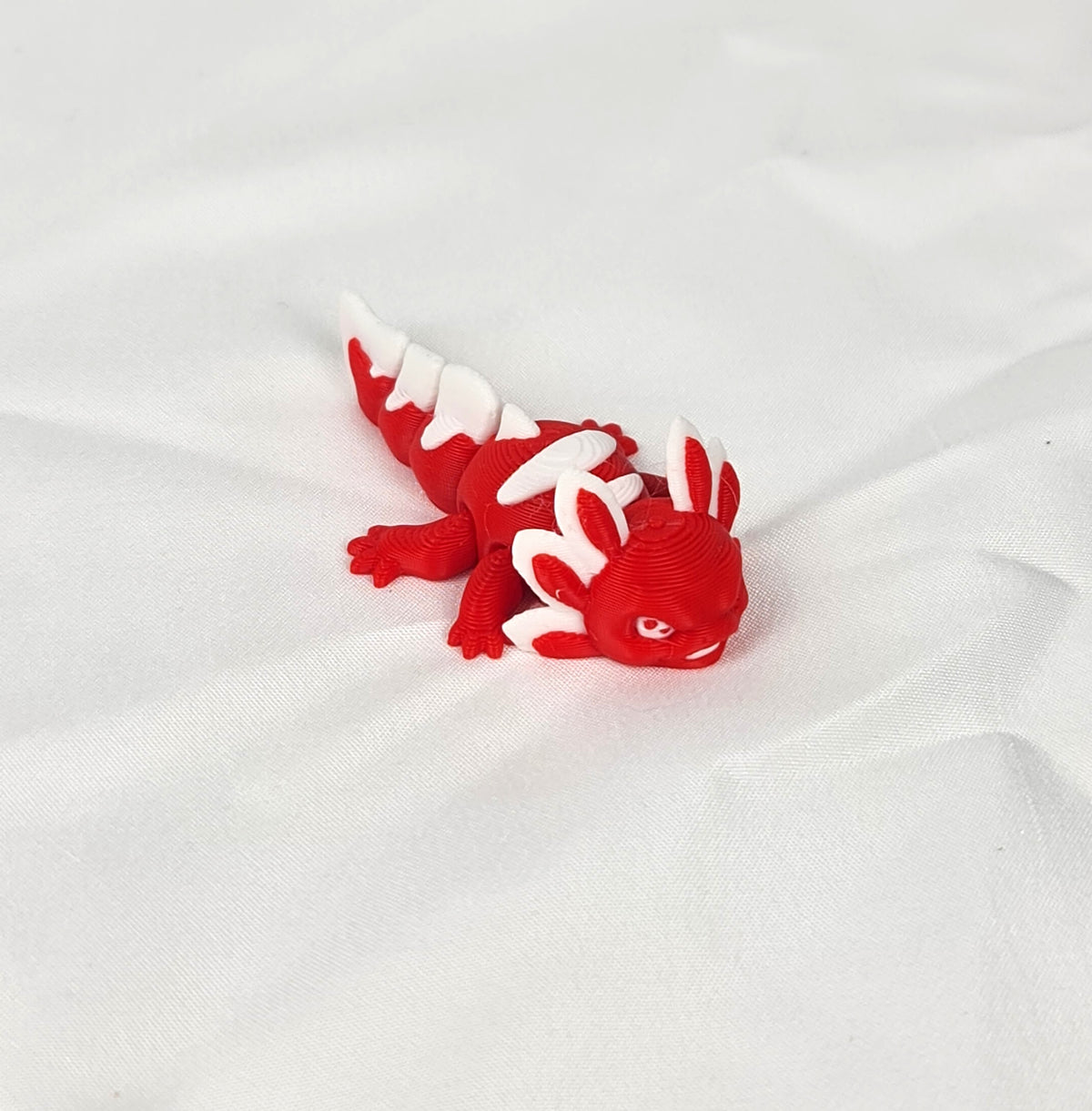 De rode en witte 3D-geprinte flexibele mini axolotl Ruby gefotografeerd vanuit een schuine hoek als decoratief kunstobject