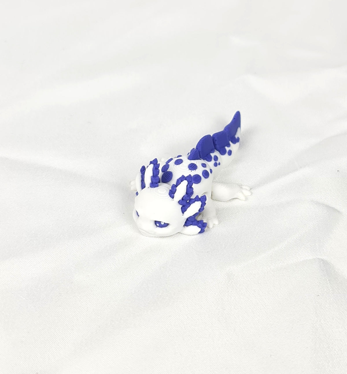 De witte en paarse 3D-geprinte flexibele mini axolotl Amethyst gefotografeerd vanuit een schuine hoek als decoratief kunstobject