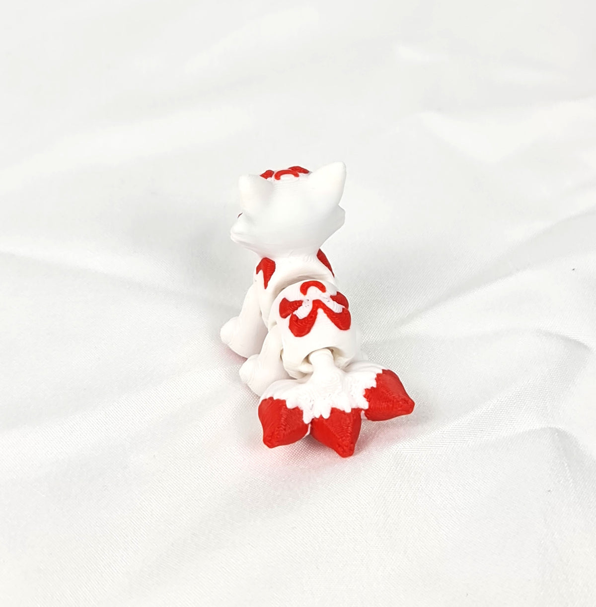 De witte en rode 3D-geprinte flexibele mini Kitsune gefotografeerd vanuit een hoek met zicht op de staart als decoratief kunstobject