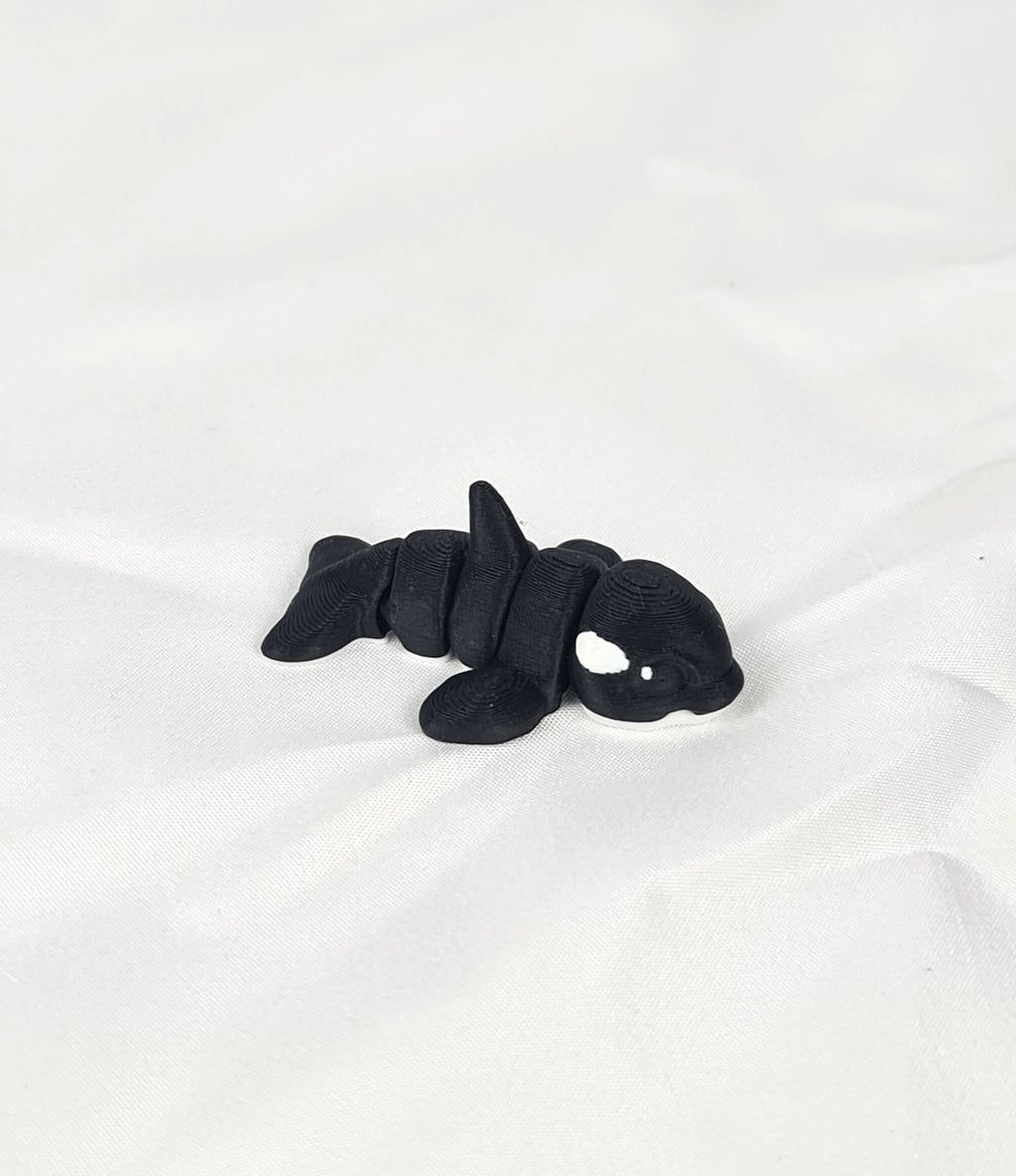 De zwart-witte 3D-geprinte flexibele mini orca gefotografeerd vanuit een schuine hoek als decoratief kunstobject