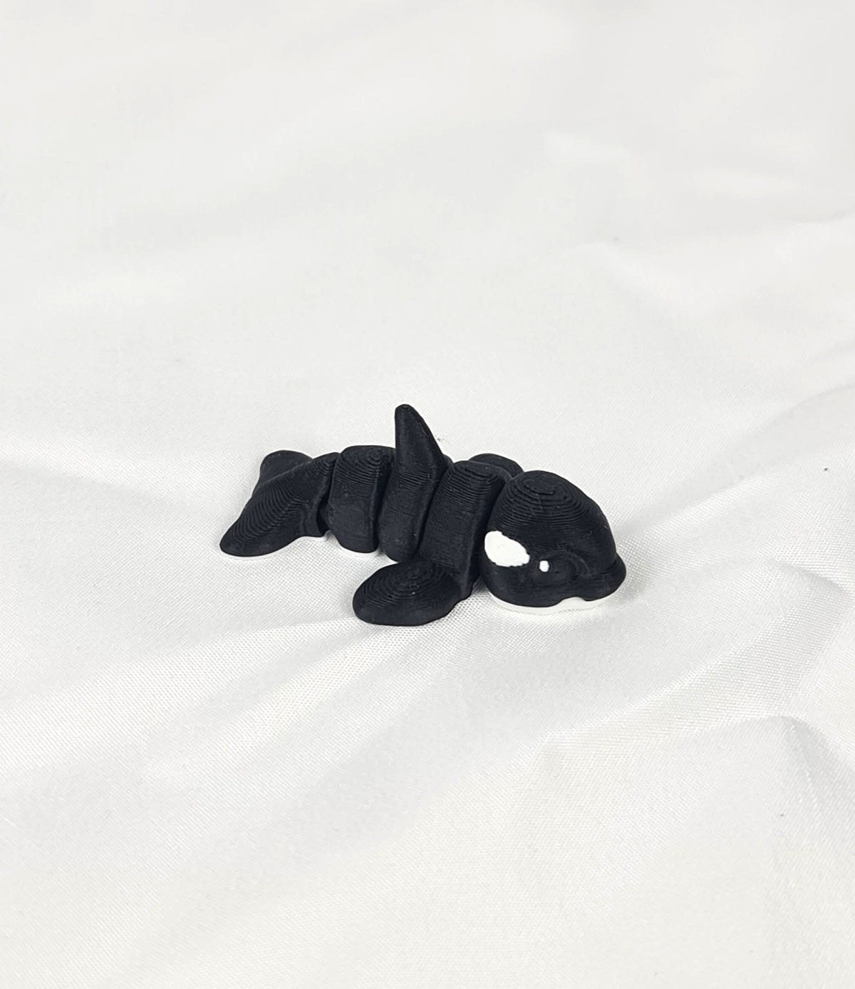 De zwart-witte 3D-geprinte flexibele mini orca gefotografeerd vanuit een schuine hoek als decoratief kunstobject